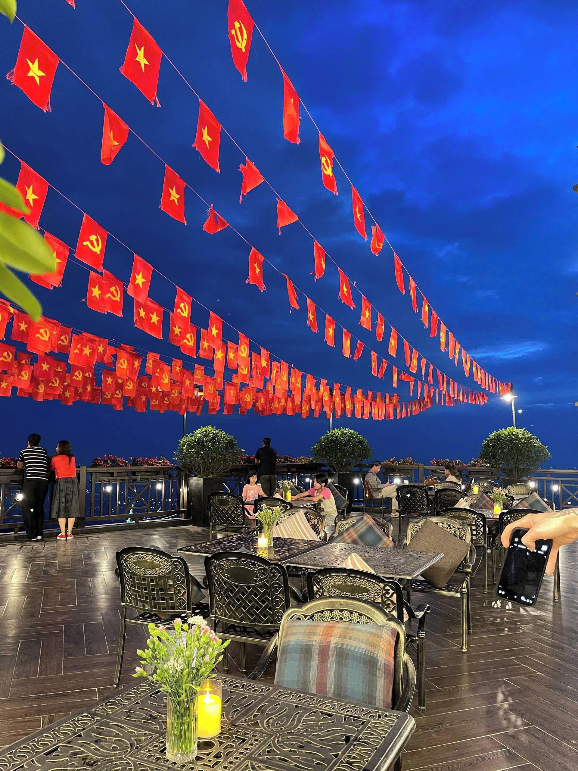 Un espacio de comedor al aire libre con mesas y sillas, decorado con banderas rojas y flores.
