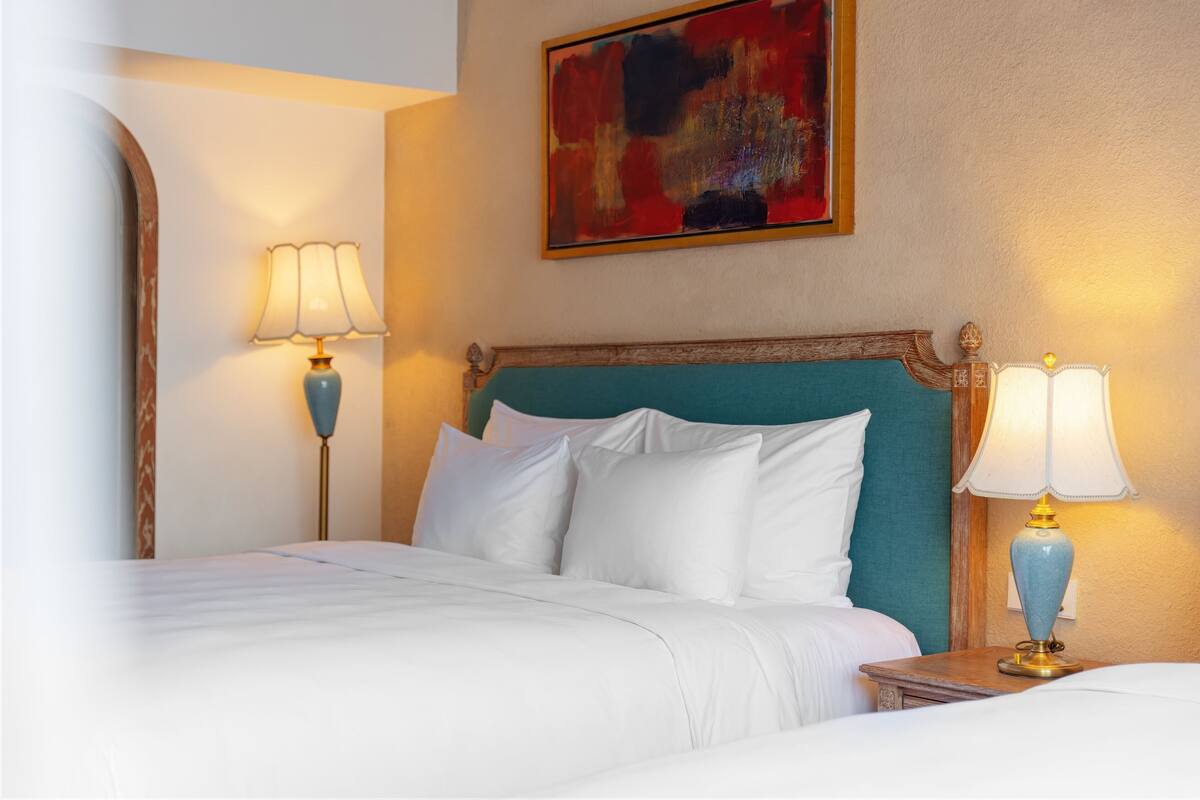 Une chambre d’hôtel avec un lit, deux lampes de chevet, un tableau au mur et une tête de lit en bois.