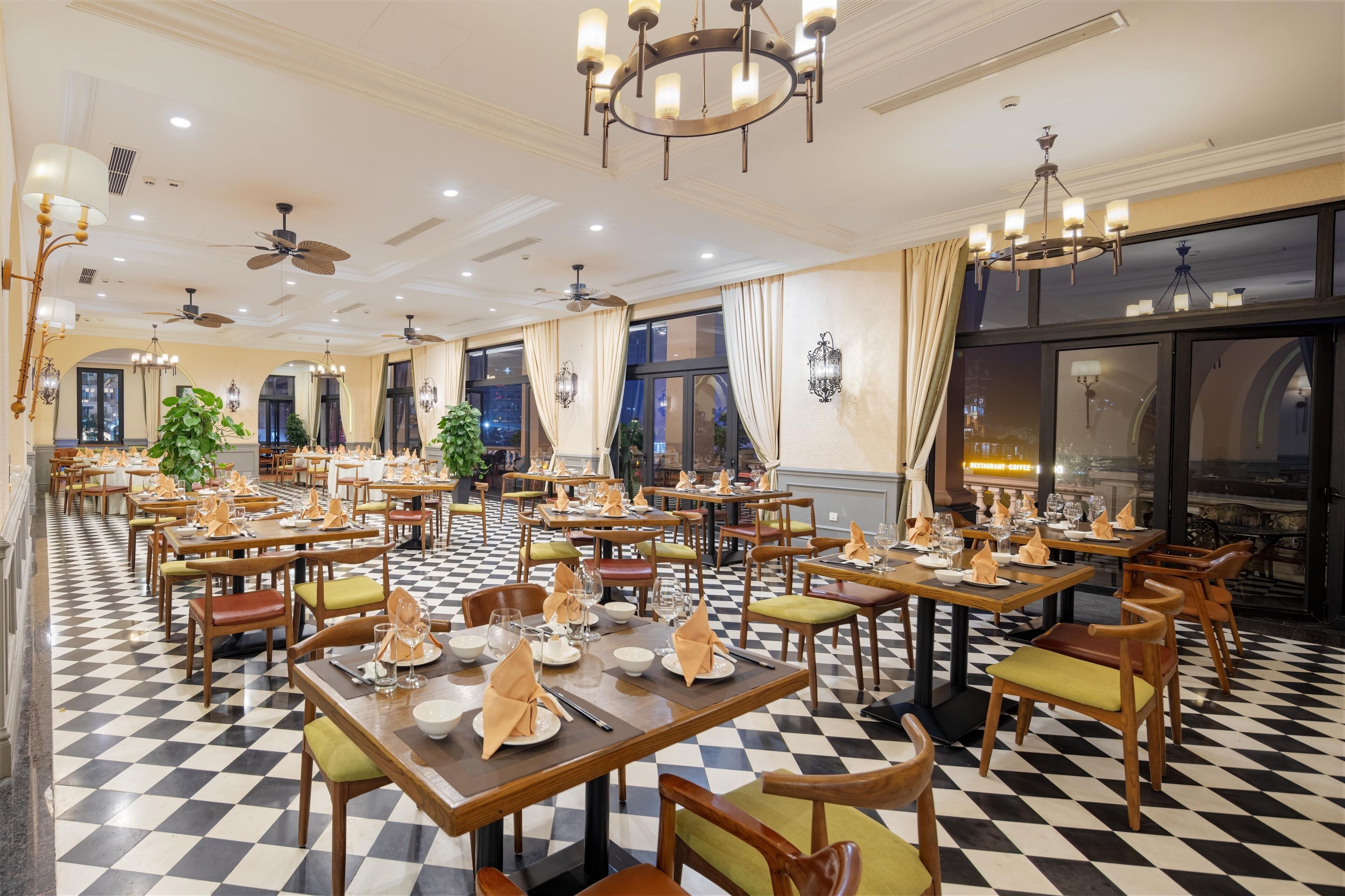 A spacious dining area with checkered flooring, multiple dining tables set with chairs, and ceiling fans.