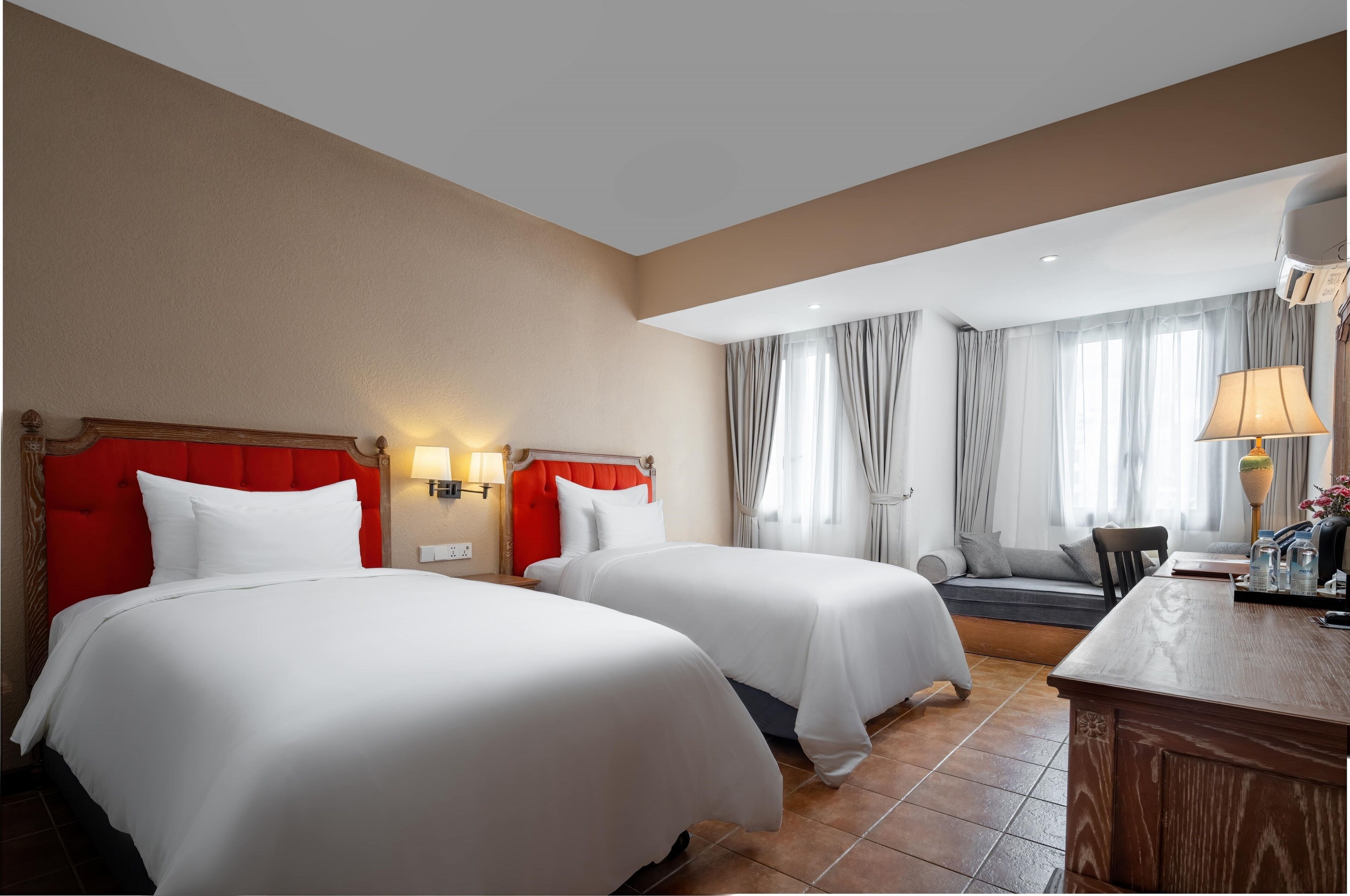 A hotel room with two beds, a desk, a chair, and a window with curtains.