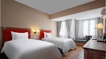 A hotel room with two beds, a desk, a chair, and a window with curtains.