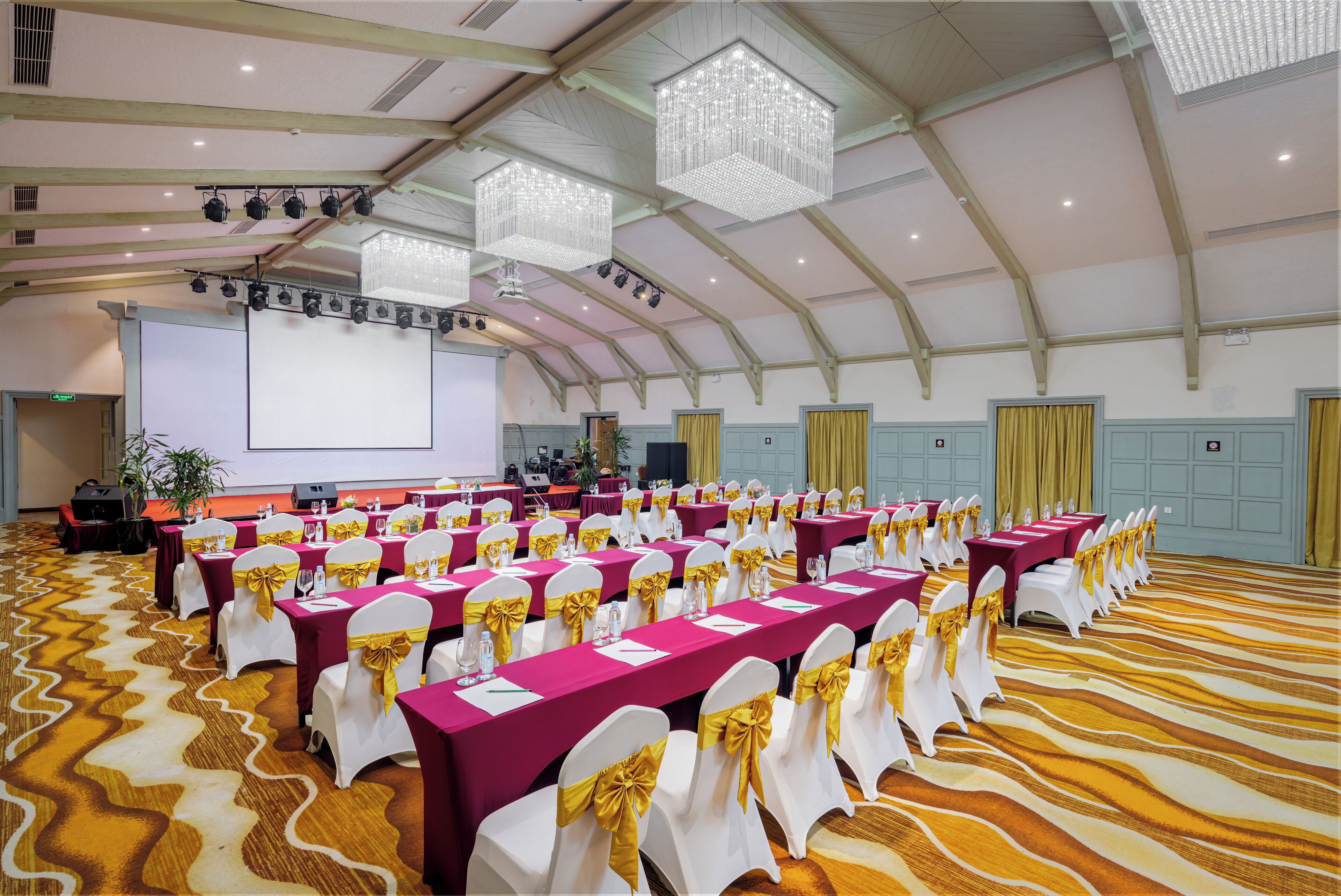 A conference room with rows of tables, chairs, and a large screen.