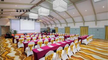A conference room with rows of tables, chairs, and a large screen.