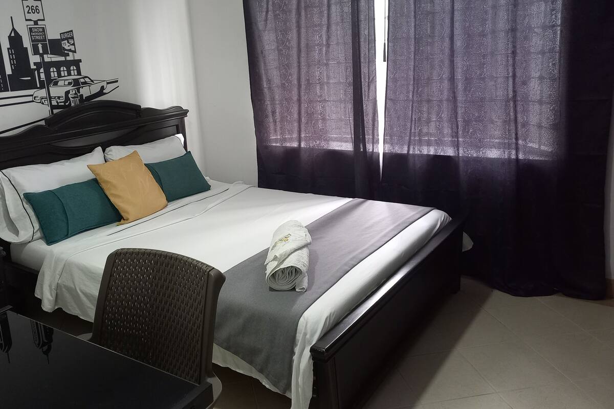 Une chambre d’hôtel avec un lit, un bureau et une chaise. Il y a une fenêtre avec des rideaux.