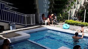 Piscina com deck ladrilhado, rodeada por espreguiçadeiras e uma piscina inflável pequena.
