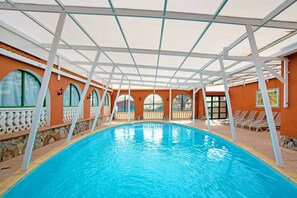Una piscina interior con zona cubierta, paredes de piedra y ventanas arqueadas.