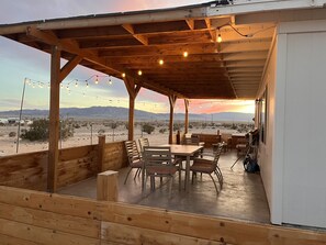 An outdoor patio with wooden furniture, string lights, and a view of a desert landscape. - 360’ views - 5 acres - stars - sunsets (Twentynine Palms)