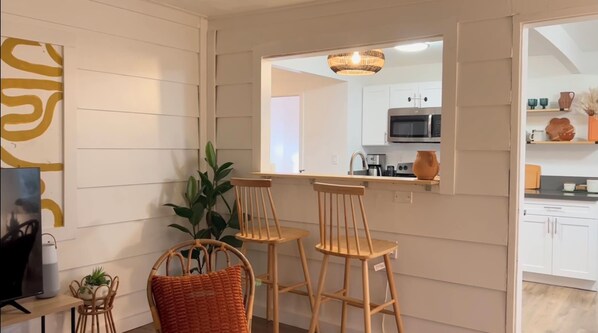 A modern kitchen with white cabinets, a microwave, and a sink. There are two wooden stools and a potted plant. - 360’ views - 5 acres - stars - sunsets (Twentynine Palms)