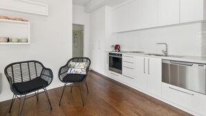 Une cuisine moderne avec des meubles blancs, un lave-vaisselle et une machine à café. On y trouve deux chaises noires avec des coussins.