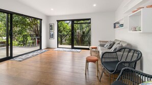 A spacious living area with large sliding glass doors leading to a balcony, a sofa, two chairs, and a coffee table. - Scotts Landing Bach Retreat - Mahurangi East (Scotts Landing)