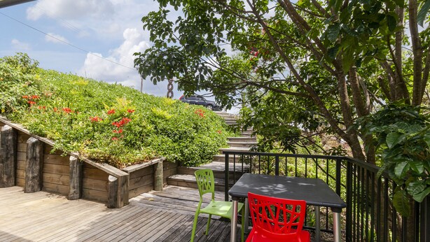 A wooden deck with a table and two chairs, surrounded by lush greenery and a staircase leading up. - Scotts Landing Bach Retreat - Mahurangi East (Scotts Landing)