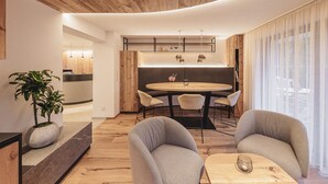 A modern living room with a round dining table, two grey armchairs, a potted plant, and a wooden ceiling.