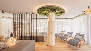 A modern lounge area with a sofa, lounge chairs, a tall column with greenery, and a patterned wall.