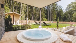 A hot tub on a wooden deck with a view of a forested area and a small building. - Silva-Apartments – Apartment "Klausberg" (St.Johann)