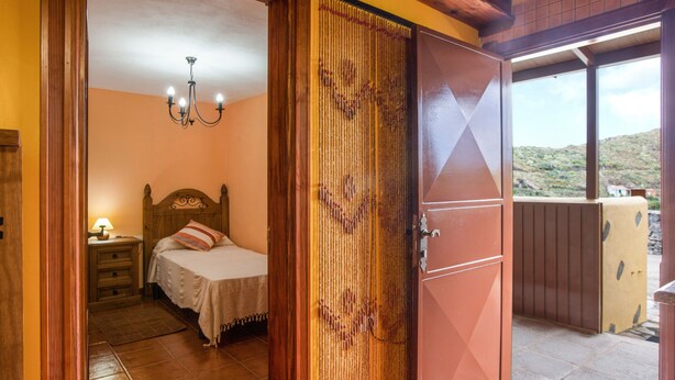 A bedroom with a bed, a nightstand, a lamp, a wooden door, and a view of the outside. - Casa Chinamada with Sea View, Mountain View, Terrace & Wi-Fi (La Laguna)