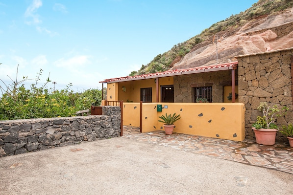 A stone building with a yellow facade, a covered porch, and potted plants.