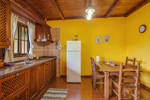 A kitchen with wooden cabinets, a white refrigerator, a dining table with chairs, and a yellow wall.