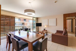 En moderne stue med spiseplads, store vinduer, et fladskærms-tv og en sofa.