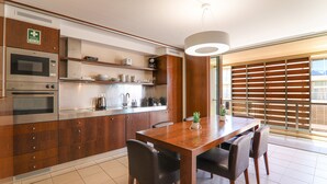 A modern kitchen with built-in appliances, a dining area with a wooden table and chairs, and a large window with blinds.