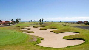 A golf course with bunkers, a clear sky, and a view of the ocean.