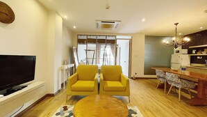 Un salon moderne avec un téléviseur à écran plat, deux fauteuils jaunes, une table basse en bois et un tapis à motifs.