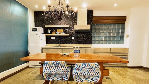 Une cuisine moderne avec une table à manger en bois et deux chaises à motifs, un four encastré et un lustre décoratif.