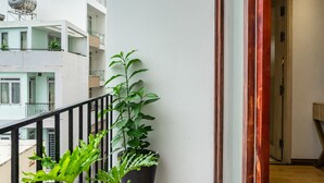 Un balcon orné de deux plantes en pot, doté d’une rambarde en métal et offrant une vue sur les bâtiments voisins.