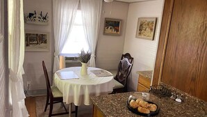 Un coin repas avec une table ronde, des chaises, un vase avec des plantes et un plateau de pâtisseries posé sur un comptoir en granit.
