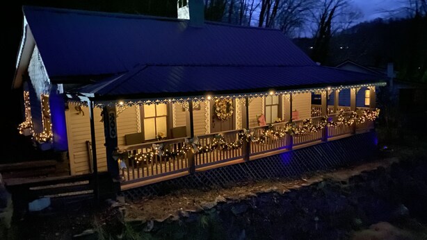 Un bâtiment doté d’un porche décoré de guirlandes lumineuses et de couronnes, d’un espace couvert avec un toit et d’un chemin piétonnier délimité par une clôture.