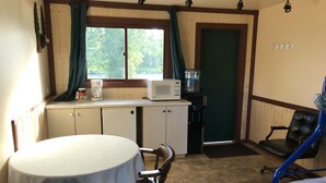 A small room with a round table, a chair, a bed, a microwave, a water dispenser, and a window with curtains.