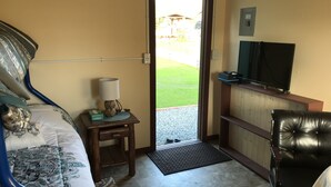 A hotel room with a bed, a desk with a lamp, a television, a chair, and a view of the outdoors.