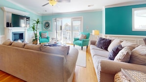 A living room with a fireplace, teal walls, and a ceiling fan. - Spacious Townhome w/Ocean Views, Elevator, Dog Friendly & Steps to Beach (Kure Beach)
