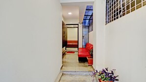 A narrow hallway with a red sofa and a small table, leading to a room with a large window and a view of the sky.