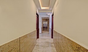 Um corredor com piso de mármore, portas de madeira e teto com iluminação embutida.