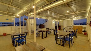 A spacious indoor area with multiple tables and chairs, a kitchen area, and a view of the cityscape.