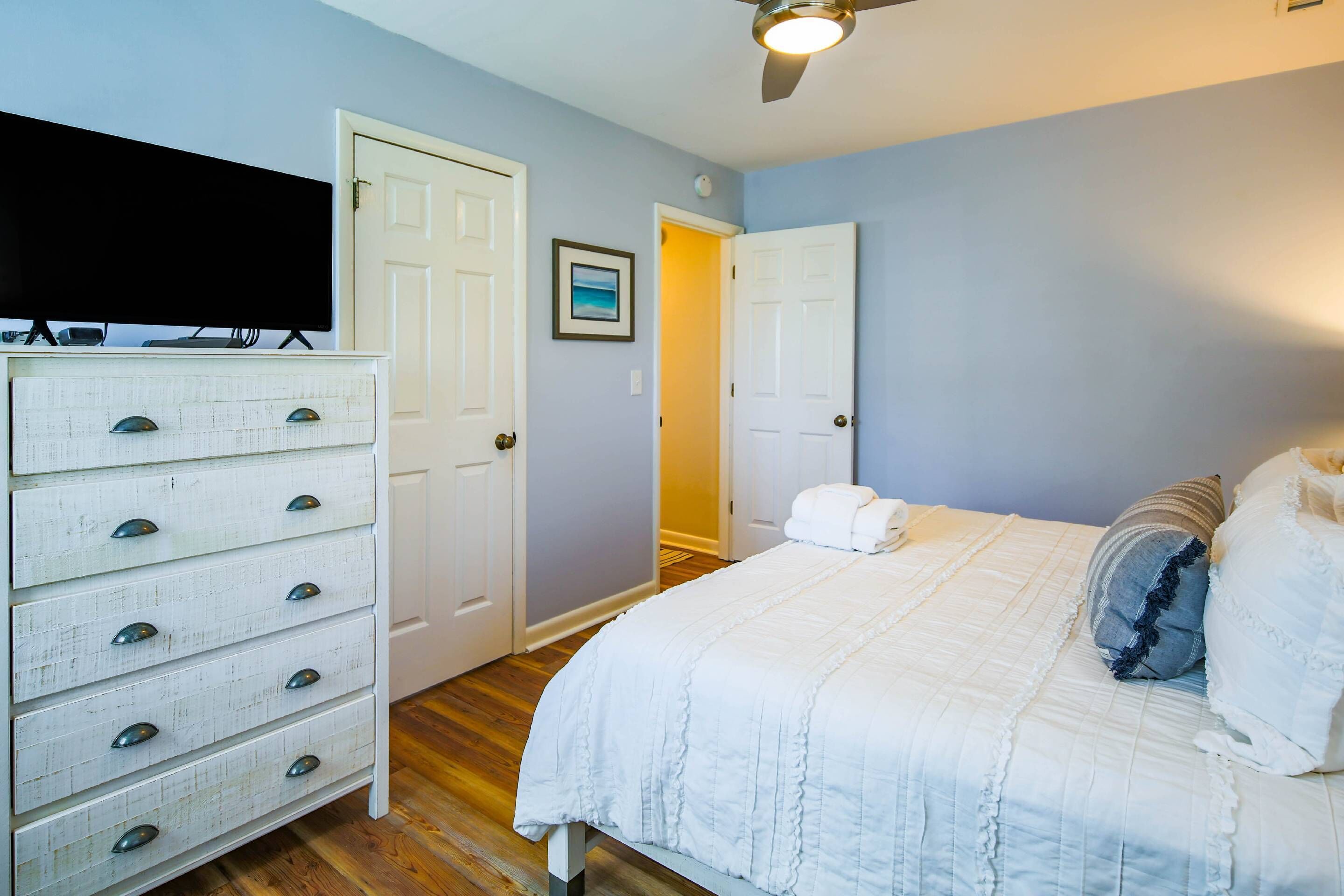 A bedroom with a bed, dresser, and a television on a stand.