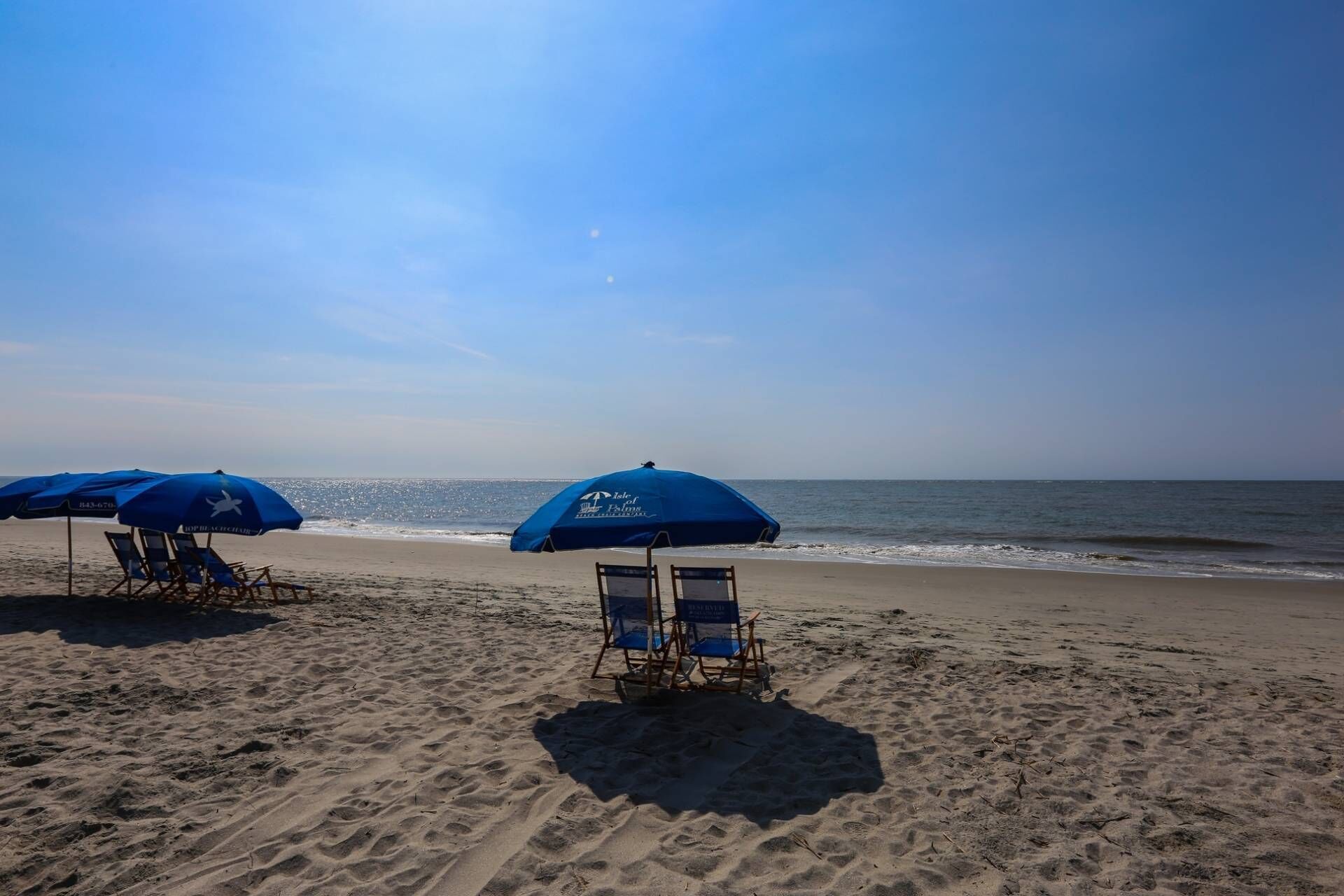 A beach with blue umbrellas and beach chairs.