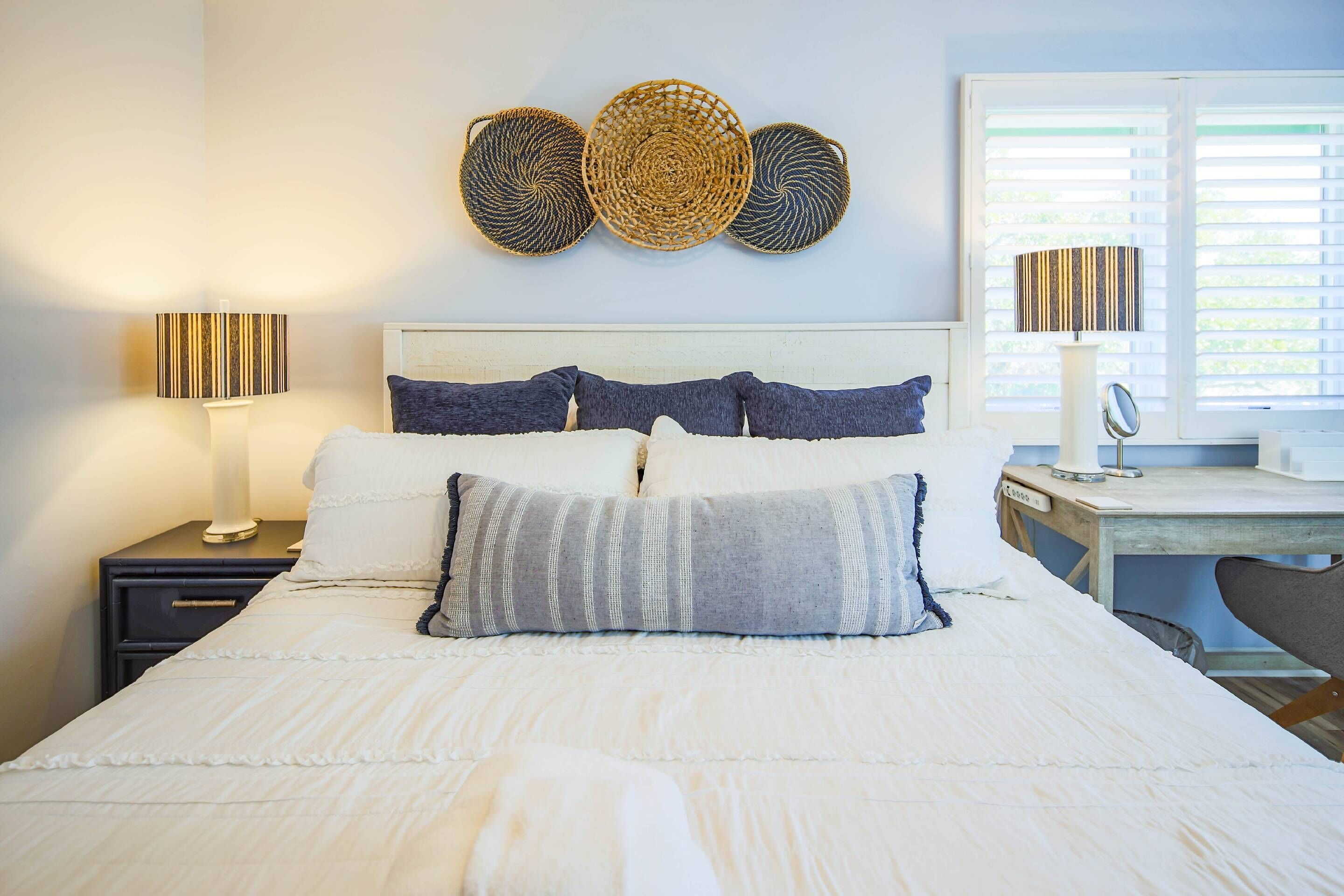 A neatly made bed with white bedding, a bedside table with a lamp, and a wall-mounted decorative basket.