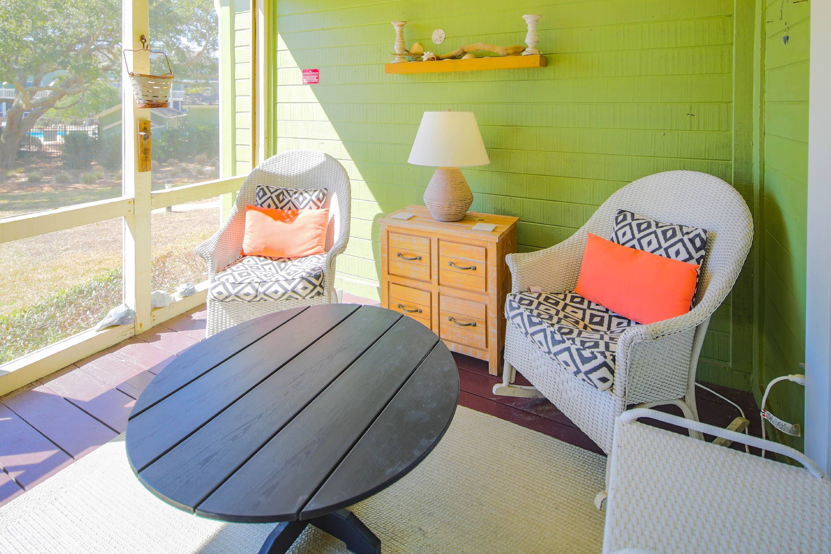 A room with two wicker chairs, a small wooden table, and a lamp on a wooden cabinet.