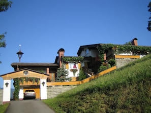 A hillside house with a car parked in front, a wooden gate, and a bell tower.