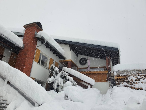 A house with a sloped roof covered in snow, a brick chimney, and a wooden deck.