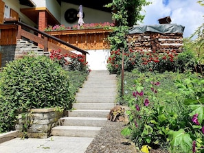 Un escalier en pierre menant à une porte en bois, entouré d’une végétation luxuriante et de fleurs aux couleurs vives.