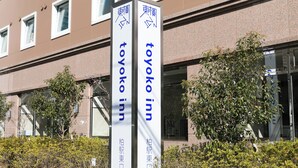 Señal de Toyoko Inn con flechas direccionales y la fachada de un edificio al fondo.