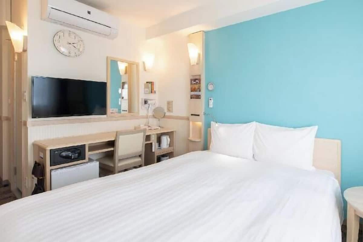 Hotellihuone, jossa on sänky, työpöytä tietokoneella, televisio ja peili.