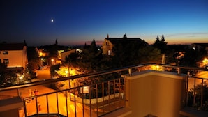A nighttime view from a balcony overlooking a residential area with houses, a street, and a crescent moon in the sky. - Hotel Terra (Novalja)