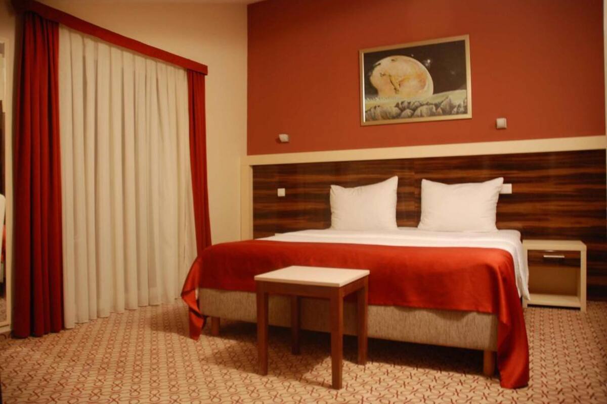 A hotel room with a large bed, a small table, a nightstand, and a painting on the wall.