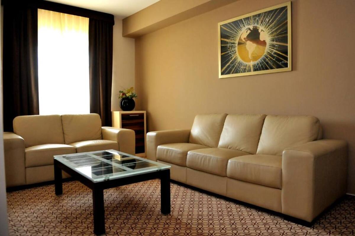 A living room with two beige sofas, a glass coffee table, a small side table with a vase, and a painting on the wall.