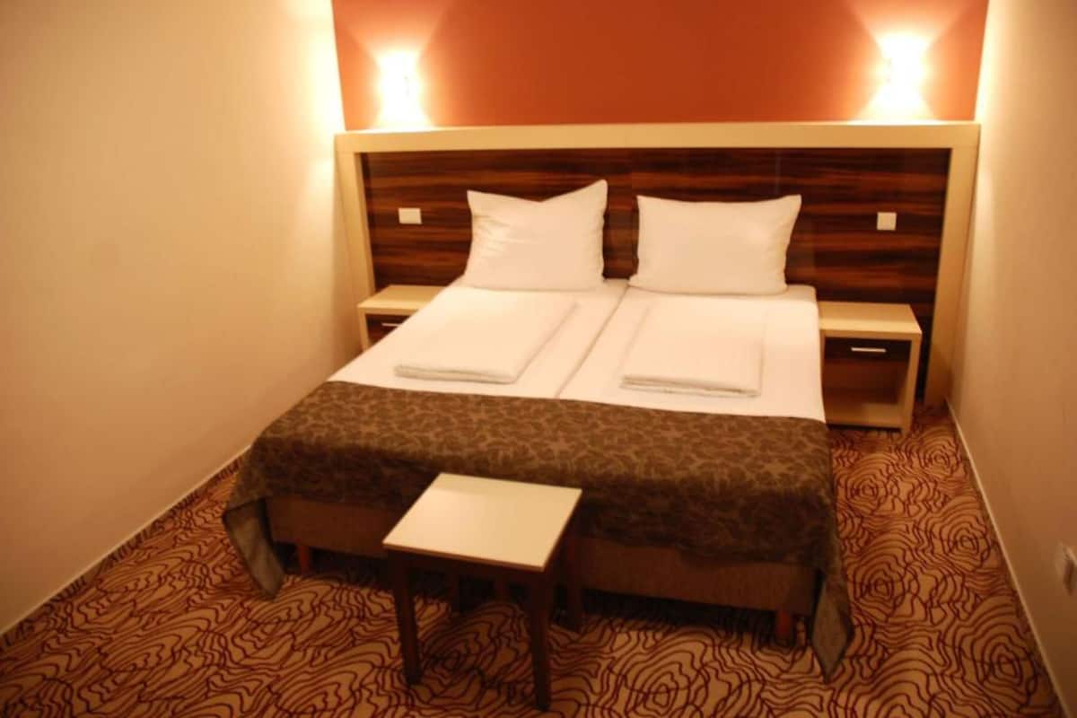 A double bed with two pillows, a bedside table, and a bench.