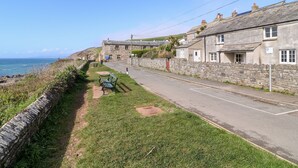 Una calle costera con casas de piedra, un banco y una vista despejada del mar.