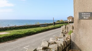 Una carretera costera con un muro de piedra y un cartel que dice "Virginia Cottage West".